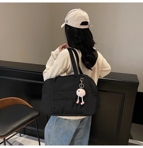 Detail of a large black canvas travel tote bag with pink fur ball charm shown on a model