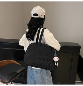 Detail of black high-capacity nylon tote bag with pink pompom charm shown on a model