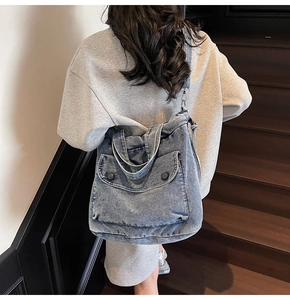 Detalle del bolso de mezclilla azul con costuras blancas y bolsillo frontal con solapa