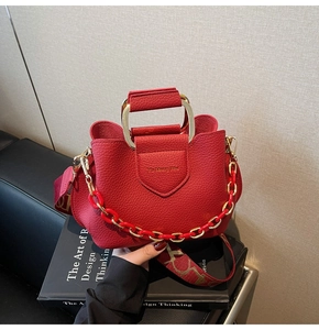 Detail of red lychee leather bucket bag with gold handle and vintage jacquard strap