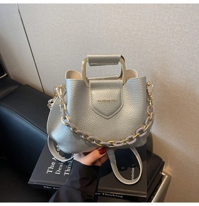 Detail of silver lychee texture handbag with golden handle and purple chain link