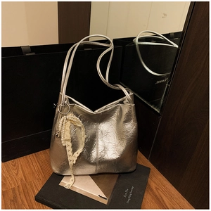 Détail d'un sac seau plissé argenté avec breloques en perles et dentelle sur livres