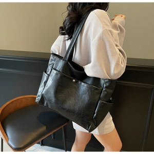 Detail of large black tote bag with vintage wrinkled texture and side pocket shown on model
