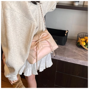 Detail shot of light pink crossbody bag featuring a large bow and elegant chain strap