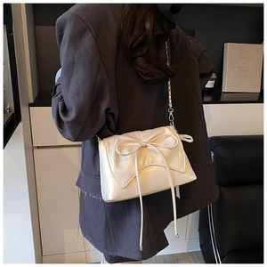 Detail of cream bow crossbody bag featuring a stylish ribbon and silver chain strap