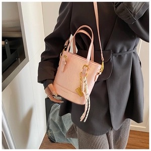 Detail of pink bucket bag with gold hardware and woven pendant on model