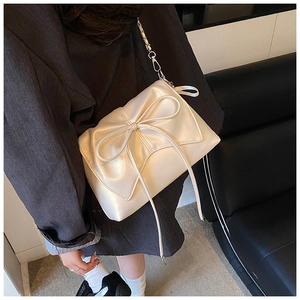 Detail of a creamy white crossbody bag with a large bow on a black blazer
