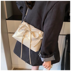 Side view of cream bow shoulder bag showing size and sleek leather texture on model