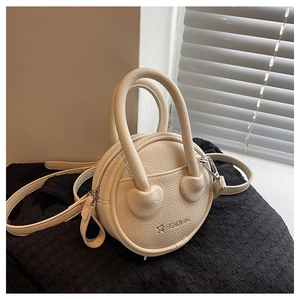 Close-up of cream textured leather mini round bag with heart-shaped handle detail