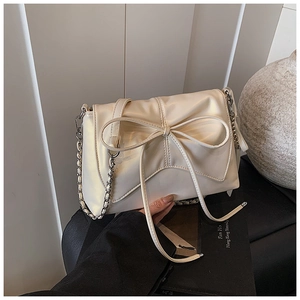 Detail of cream ballet-style bag featuring a large bow and silver chain strap
