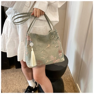 Dettaglio borsa tote in seta verde chiaro con ricami classici e nappa bianca elegante