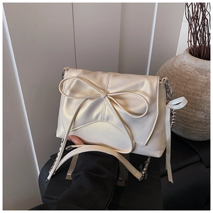 Detail of off-white ballet-style crossbody bag featuring a large bow and silver chain strap
