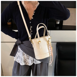 Close-up of cream-white bucket bag with dual handles and woven rope tassel detail