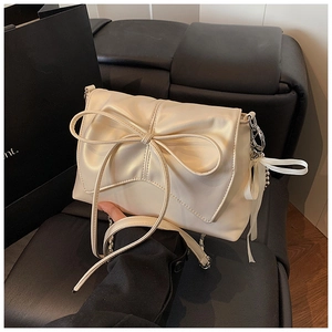 Detail of a creamy white bow square bag with a chain strap on a black leather seat