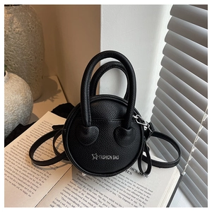 Detail of black mini round crossbody bag with lychee texture on an open book