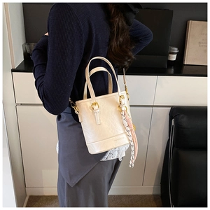 Detail view of cream bucket bag in pebble leather with silk scarf and gold hardware