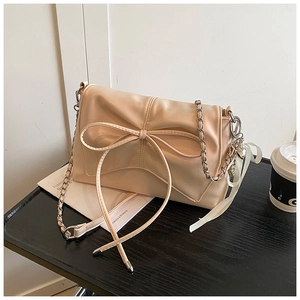 Detail of beige bow crossbody bag with silver chain strap and heart charm on table