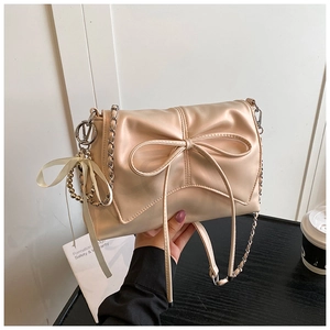 Close-up of champagne bow shoulder bag with glossy leather, metal chain and bead charm