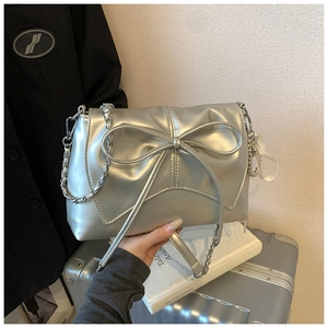 Detail of silver metallic handbag featuring a large bow and chain strap in hand