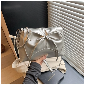 Detail of silver crossbody bag with a large bow and metallic chain strap in a lifestyle setting