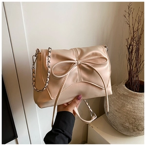 Close-up of a stylish beige bow crossbody bag featuring a golden chain strap and leather finish