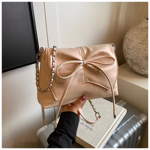 Close-up of elegant beige shoulder bag with bow detail and metal chain strap