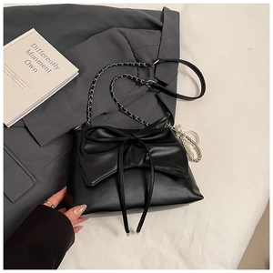 Close-up of black crossbody bag with large bow and silver bead detail on fabric background