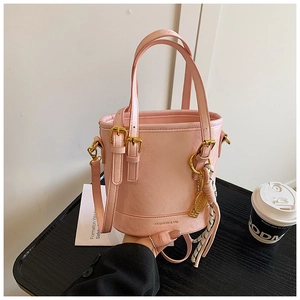 Detail of pink bucket bag featuring golden racket charm and striped silk scarf accessory