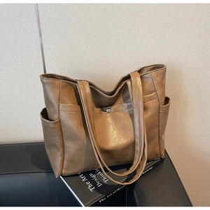 Detail of a brown tote bag featuring side pockets and snap button on a leather sofa