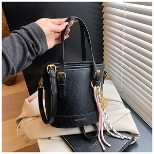 Detail of black textured leather bucket bag with gold hardware and woven pendant