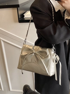 Metallic silver crossbody bag with a large bow detail and chain strap worn by a model