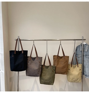 Bolsos tote grandes de lona en varios colores con asas de cuero en un soporte de exhibición