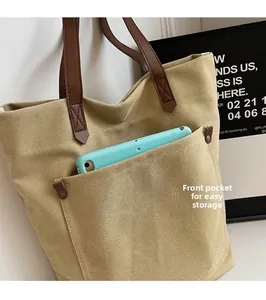 Detalle de bolso de lona caqui con bolsillo frontal grande y asas de cuero marrón