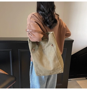 Detalle del bolso tote de lona verde oliva con correas de cuero marrón y bolsillo frontal