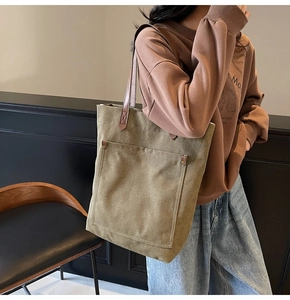 Detalle del bolso tote de lona caqui con correas de cuero marrón y bolsillo frontal