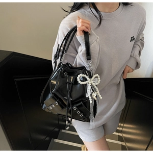 Détail du sac seau en cuir verni noir avec œillets métalliques et breloque nœud perlé