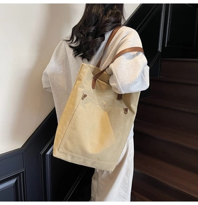 Bolso tote de lona caqui con asas de cuero marrón y detalle de bolsillo frontal con remaches
