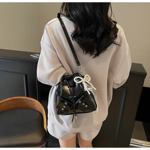 Détail d'un sac seau noir brillant avec œillets argentés et breloque noeud en perles