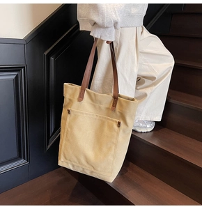 Detalle de bolso tote de lona beige con asas de cuero marrón y remaches de metal vintage