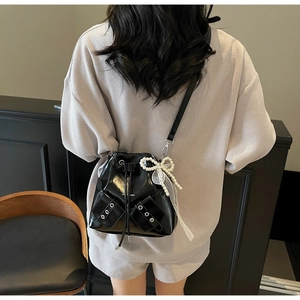 Détail d'un sac seau brillant noir avec nœud en perles, tulle blanc et œillets métalliques