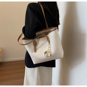 Detail of cream tote bag with brown handles and a cute elephant charm on a model's shoulder