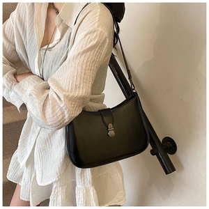 Detail of a black leather saddle bag featuring a vintage metal clasp on a model shoulder