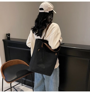 Detalle de un bolso tote de lona negra grande con correa ancha marrón llevado por una modelo