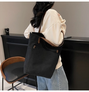 Detalle de bolso tote de lona negra con correas de cuero marrón y bolsillo exterior