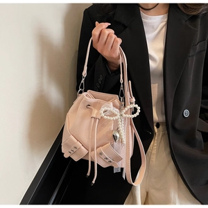 Détail du sac seau en similicuir rose avec nœud perlé, breloque cœur et rivets déco