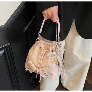 Détail du sac seau rose à cordon avec breloque nœud en perles et texture PU lisse