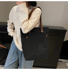Detalle de bolso tote de lona negra con asas de cuero marrón y bolsillo con remaches