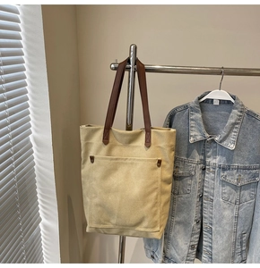 Detalle de bolsa tote de lona con asas de cuero marrón y remaches metálicos reforzados