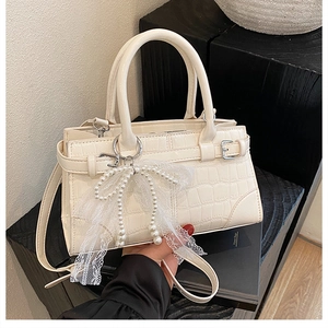 Détail du sac seau crème à texture crocodile avec nœud en dentelle et perles