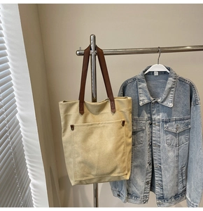 Detalle de bolso tote de lona con bolsillo frontal y asas de cuero marrón en percha